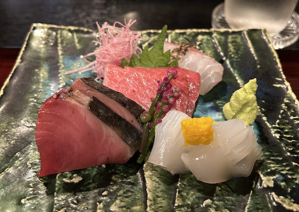 色とりどりの刺身が盛り付けられた皿。魚、わさび、紫の飾り物が見える。